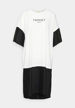 Robe ample blanche et noire avec manches courtes plissées noires et ourlet inférieur plissé, "TWINSET MILANO" imprimé sur la poitrine.