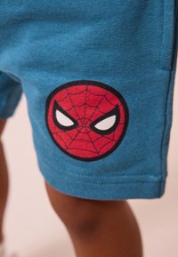 Blå bomuldsshorts med en stor rød og sort Spider-Man logo med hvide øjne, tydeligt placeret på venstre nederste ben.