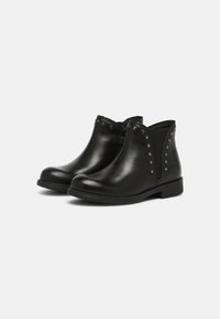 Botas de tobillo de cuero negro con una textura suave, paneles laterales elásticos y tachuelas plateadas a lo largo de los bordes. Tacón bajo en bloque y diseño de punta redondeada.