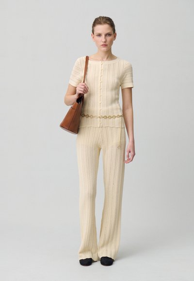 Ensemble en tricot à deux pièces de couleur beige clair avec un motif texturé, haut à manches courtes et pantalon évasé, associé à un sac à épaule marron.