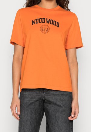 Persoon draagt een oranje T-shirt met korte mouwen met de tekst "WOOD WOOD" en een klein zwart embleem op de borst, gecombineerd met donkere jeans.