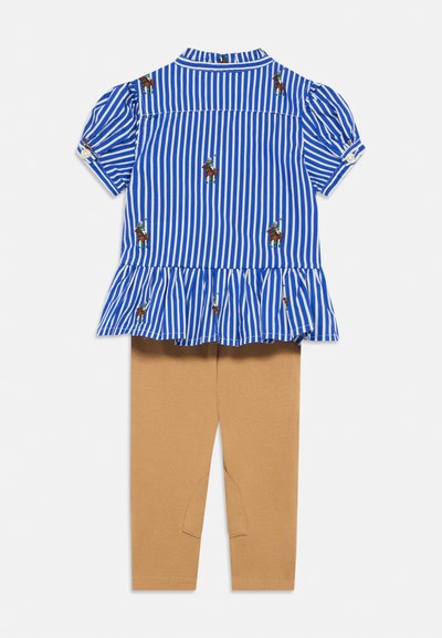 Μπλε και λευκό ριγέ κοντομάνικο τοπ με βολάν στο τελείωμα και κεντητά μοτίβα αλόγων, συνδυασμένο με καφέ κολάν με επιδιορθώσεις στα γόνατα.