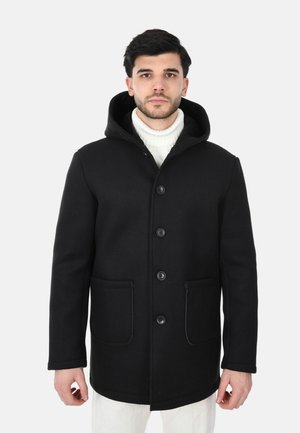 Cappotto nero con cappuccio in misto lana, con chiusura a bottoni, due tasche frontali e un maglione a collo alto a costine, testurizzato, indossato sotto.