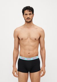 Schwarze Baumwoll-Boxershorts mit einem hellblauen Hosenbund, der mit pinkem "HUGO"-Branding versehen ist. Klassische Passform und glatte Textur.