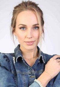 Gouden ketting en armband met een kleine heldere edelsteen, gedragen over een versleten spijkerjasje met gerimpelde mouwen.