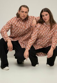 Dos modelos vestidos con camisas de manga larga a juego con un patrón geométrico en naranja y blanco, combinadas con pantalones negros y zapatillas blancas.
