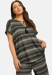 Top a zigzag grigio e nero con scollatura a V e maniche corte. Presenta una chiusura con coulisse e un dettaglio a nappina. Vestibilità ampia.