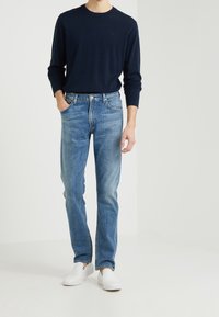 Granatowa koszula z długim rękawem, jasnoniebieskie jeansy o prostych nogawkach oraz białe buty wsuwane. Jeansy mają klasyczny design z pięcioma kieszeniami i wyblakły odcień.