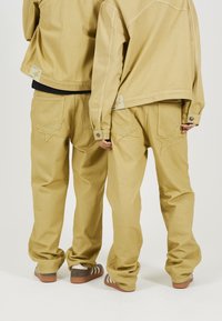 Tan denim jacket and pants, both with star-shaped stitching on back pockets. Relaxed fit, soft texture, and button accents on jacket cuffs.