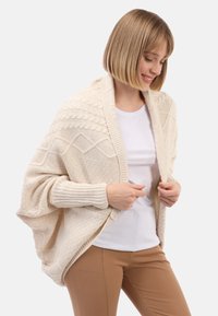 Kimono stylizovaný cardigan v krémové barvě, s texturovanými pletenými vzory a žebrovanými rukávy. Otevřený design se volnou a splývavou siluetou.