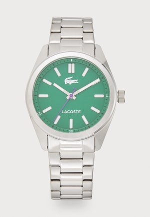 Montre Lacoste avec un cadran vert, un bracelet en acier inoxydable argenté, des index horaires blancs et une aiguille des secondes violette. Comprend un logo et un indicateur de date.