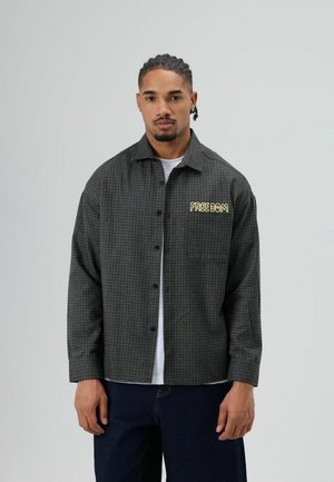 Donkergroene geruite overhemd met een losse pasvorm, voorzien van een geel geborduurd "FREEDOM"-tekst op het linkerborstzakje.