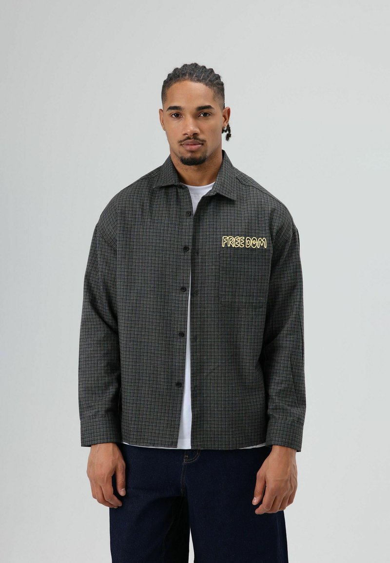 Donkergroene geruite overhemd met een losse pasvorm, voorzien van een geel geborduurd "FREEDOM"-tekst op het linkerborstzakje.