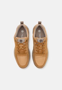 Zapatillas marrones que combinan materiales de ante y malla, con punta redondeada, cuello acolchado y cordones en contraste con una lengüeta con logo.