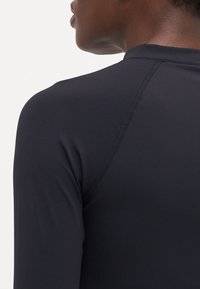 Black long-sleeve activewear top with a fitted design, smooth texture, and flat seams, showcasing a high neckline and raglan sleeves.