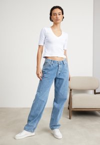 Haut court à manches courtes côtelé blanc associé à un jean en denim large bleu clair et des baskets blanches. Remarquable coupe décontractée et design simple.