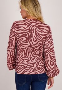 Lange mouwen blouse in roze en bordeaux met een draaiend zebrapatroon. Heeft een relaxte pasvorm en details met elastische manchetten.