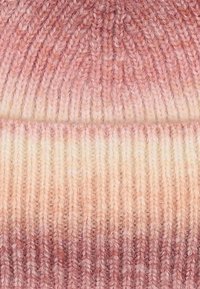 Berretto lavorato a maglia in sfumature di rosa e crema. Presenta una texture a costine con un aspetto morbido e accogliente e una cima senza cuciture.