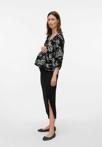 Blouse noire à fleurs avec un col en V et des manches amples, associée à une jupe noire avec des accents en dentelle et une fente sur le côté. Des ballerines noires sont portées.