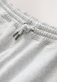 Jasnoszare spodnie dresowe z elastycznym pasem i zawiązywanym sznurkiem z metalowymi końcówkami.