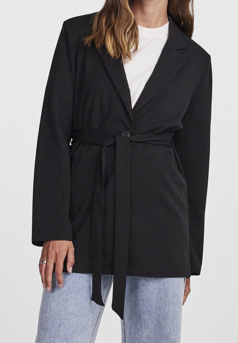 Černé sako s páskem v pase, dlouhými rukávy, klopovým límcem, jednobotonovým zapínáním a hladkým materiálem, spárované se světlými džíny.