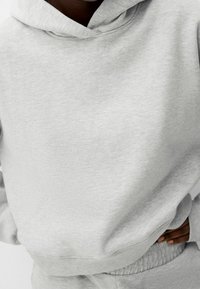 Sudadera de algodón gris con capucha ajustable, puños y dobladillo acanalados; presenta una textura suave y un corte relajado. Combina con pantalones de chándal a juego.