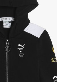 Svart zip-up hoodies med en känguruficka. Har vita axelaccent, Puma- och Sonic-logotyper, samt texturerat tyg. Silver zip-dragare.