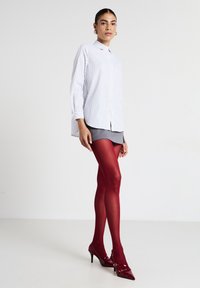 Camicia bianca con righe blu, abbinata a una minigonna grigia e calze trasparenti rosse. Scarpe con tacco rosso lucido completano l'outfit.