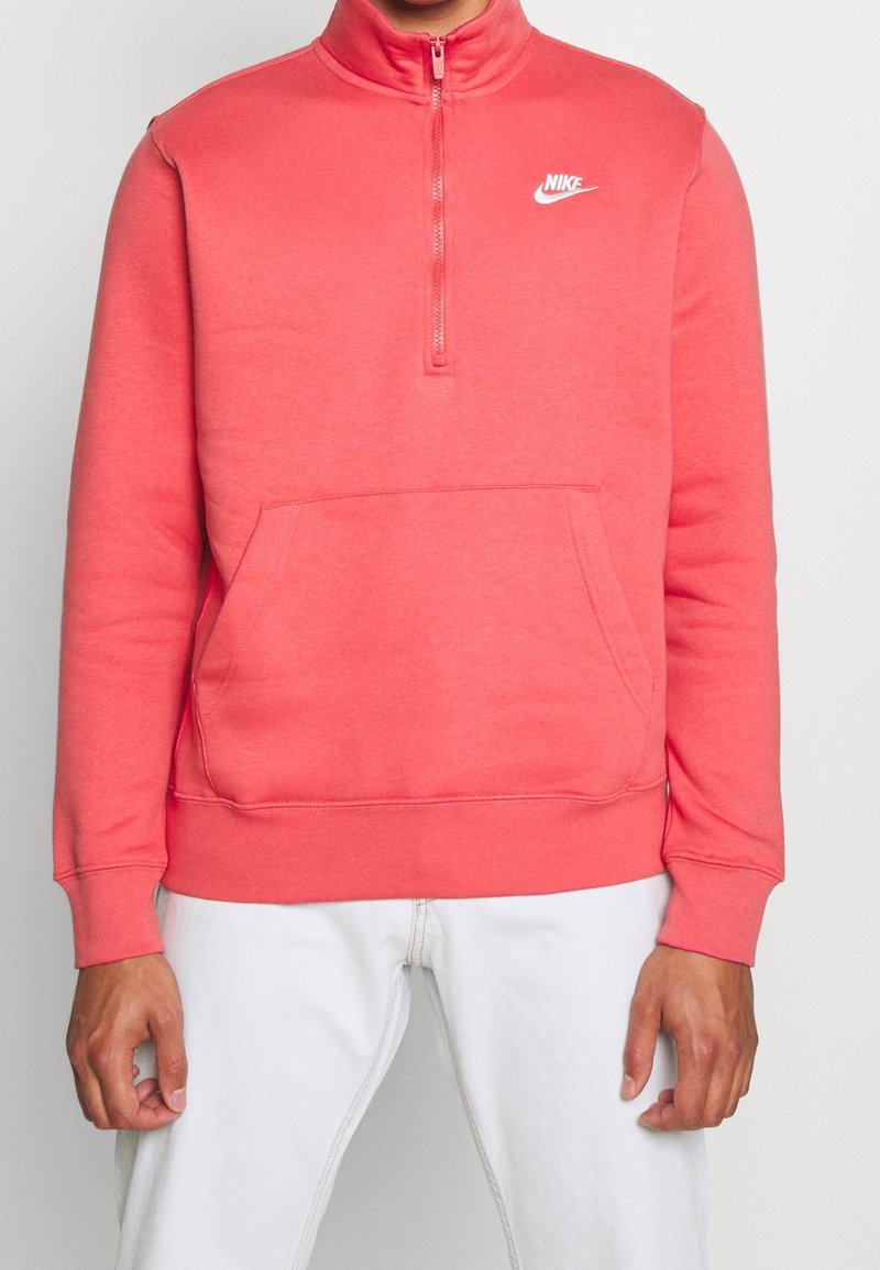 Nike zip-up-tröja i ljus korall, med hög krage, långa ärmar och en framlänges känguruficka. Mjuk tygstruktur.
