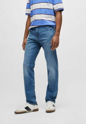 Vaqueros de mezclilla azul con un corte recto, con un diseño clásico de 5 bolsillos y un ligero desgaste. Combinados con una camiseta a rayas azul y blanca.