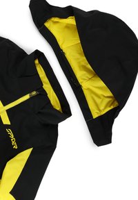 Schwarz-gelbe wasserdichte Jacke mit abnehmbarem Kapuzen, Reißverschluss und kontrastierendem Innenfutter; ausgestattet mit Logo-Detail und verstellbaren Komponenten.