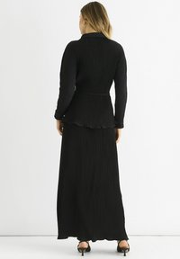 Black ribbed dress with a peplum waist and long sleeves; features a flowing skirt and simple straps on heeled shoes.