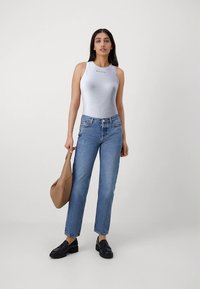 Ανοιχτό μπλε μπλουζάκι χωρίς μανίκια, μπλε τζιν με ίσια γραμμή, μαύρα μοκασίνια και μια ταμπά τσάντα ώμου. Λείο ύφασμα με λεπτή λεπτομέρεια λογότυπου στο μπλουζάκι.