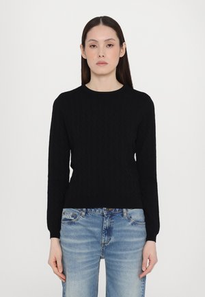 Schwarzer Strickpullover mit einem strukturierten Rautenmuster, Rundhalsausschnitt und langen Ärmeln, kombiniert mit hellblauen, ausgewaschenen Jeans.
