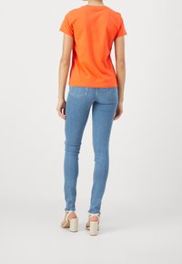 Oranžové bavlněné tričko s krátkým rukávem, spárované se světle modrými skinny džíny. Významné prvky zahrnují třepený lem a béžové sandály na blokovém podpatku.