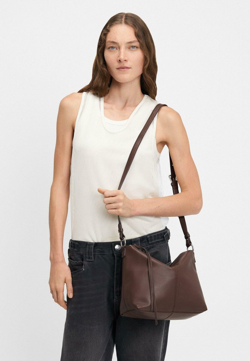 Brązowa skórzana torebka o luźnym fasonie, z długim regulowanym paskiem, minimalistycznymi akcentami i gładką teksturą.