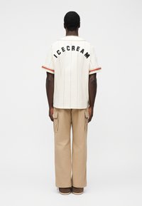 Λευκό κοντομάνικο πουκάμισο με μαύρα γράμματα "ICECREAM" στην πλάτη, με κόκκινες ρίγες. Συνδυασμένο με μπεζ παντελόνι τύπου cargo.