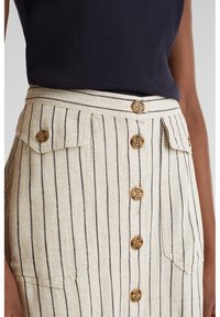 Jupe beige avec fines rayures noires verticales, fermeture à boutons devant avec cinq boutons marron, et deux poches à rabat à la taille.