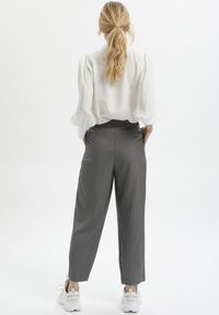 Lekka biała bluzka z bufkami, zestawiona z szarymi spodniami w prążki. Stylizacja charakteryzuje się luźnym krojem i została uzupełniona białymi sneakersami.