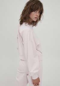 Felpa rosa chiaro con vestibilità ampia, polsini a costine e scollatura rotonda. Indossata con pantaloni affusolati abbinati, che mostrano una morbida trama di cotone.