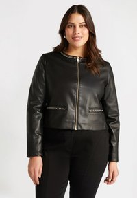 Chaqueta corta de cuero negra con cierre con cremallera en la parte delantera, cuello adornado y detalles en tono plateado en los bolsillos. Textura lisa, diseño ajustado.