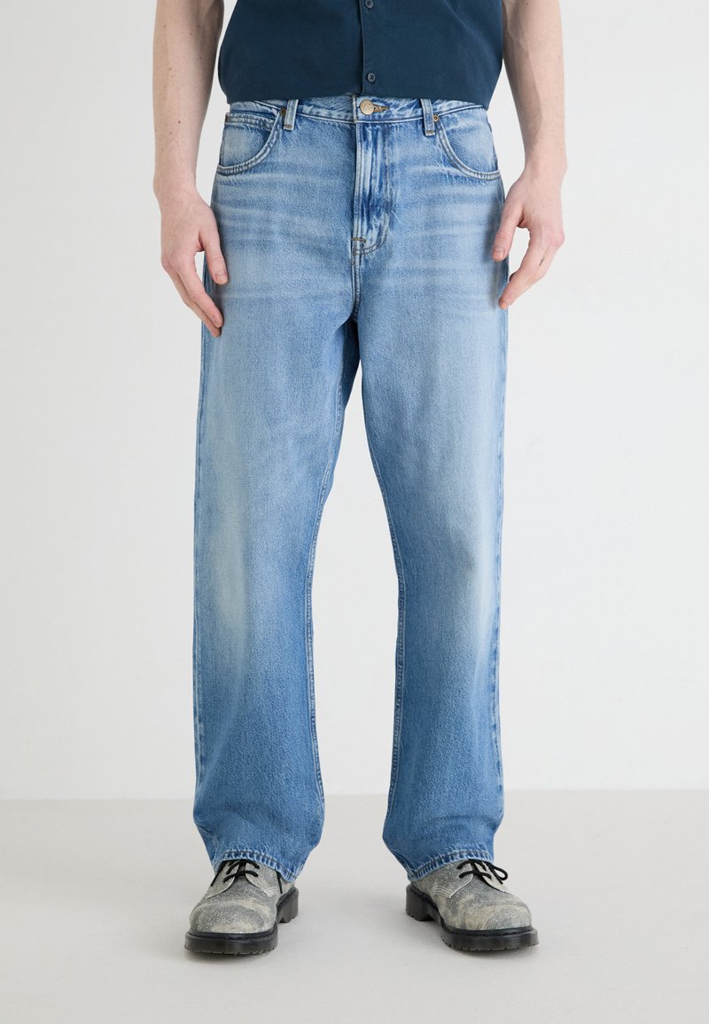 Jean en denim bleu clair avec une coupe ample, comportant un délavage, un design traditionnel à cinq poches et une fermeture à bouton à la taille.