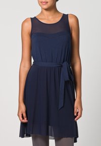 Robe sans manches bleu marine avec un corsage transparent, taille cintrée et ceinture à nouer. Matériau doux, silhouette fluide et ourlet au genou.