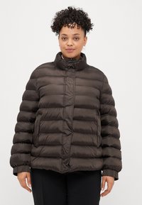 Rjava napihljiva jakna z visokim ovratnikom, ki ima vodoravno šivanje in elastične manšete. Gladek, sijoč material z kvadratno silhueto.