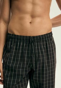 Czarne piżamowe spodnie w kratkę z elastycznym paskiem w talii, zapięciem na sznurek i siatką w kontrastowym jasnym kolorze. Miękka tekstura materiału.