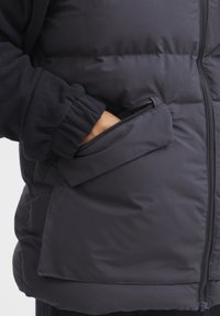 Črna izolirana brezrokavnik z gladkim zunanjim delom, notranjostjo iz flisa, elastičnimi mansetami in stranskim žepom z zadrgo.