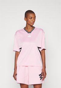 Camiseta deportiva rosa con escote en V, ribete negro y detalles negros en un diseño deportivo; combinada con pantalones cortos rosas a juego.