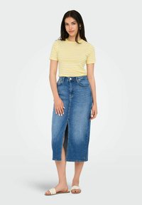 Kollane ja valge triibuline lühikeste varrukatega T-särk, mida on kombineeritud keskpika sinise denim seeliku ning esiseeliku lõhiku ja heledate sandaalidega.