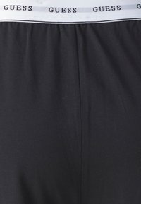 Sorte boksershorts i stoffet med bred elastisk midje med gjentatt "GUESS"-bokstaver i hvitt. Myk tekstur med et enkelt design.