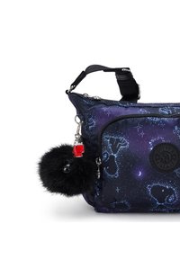 Mørkeblå crossover-taske med stjernebilleder, en sort fluffy nøglering og en lille rød huscharms hængende på den sidezipper.